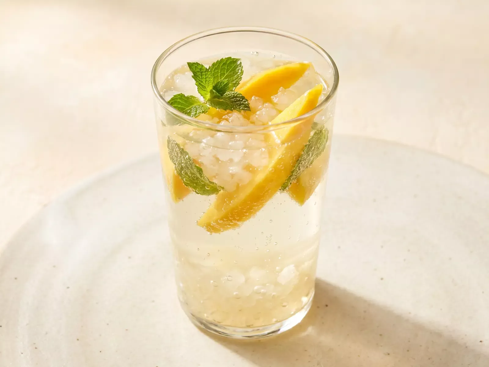 Glas waterkefir met mango en munt op een lichte ondergrond, zacht bruisend onder warme bovenverlichting