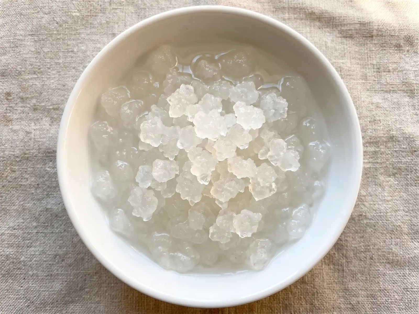 water kefir drink Transparante waterkefirkorrels in een witte kom op ruw linnen, met helder water in zacht bovenlicht