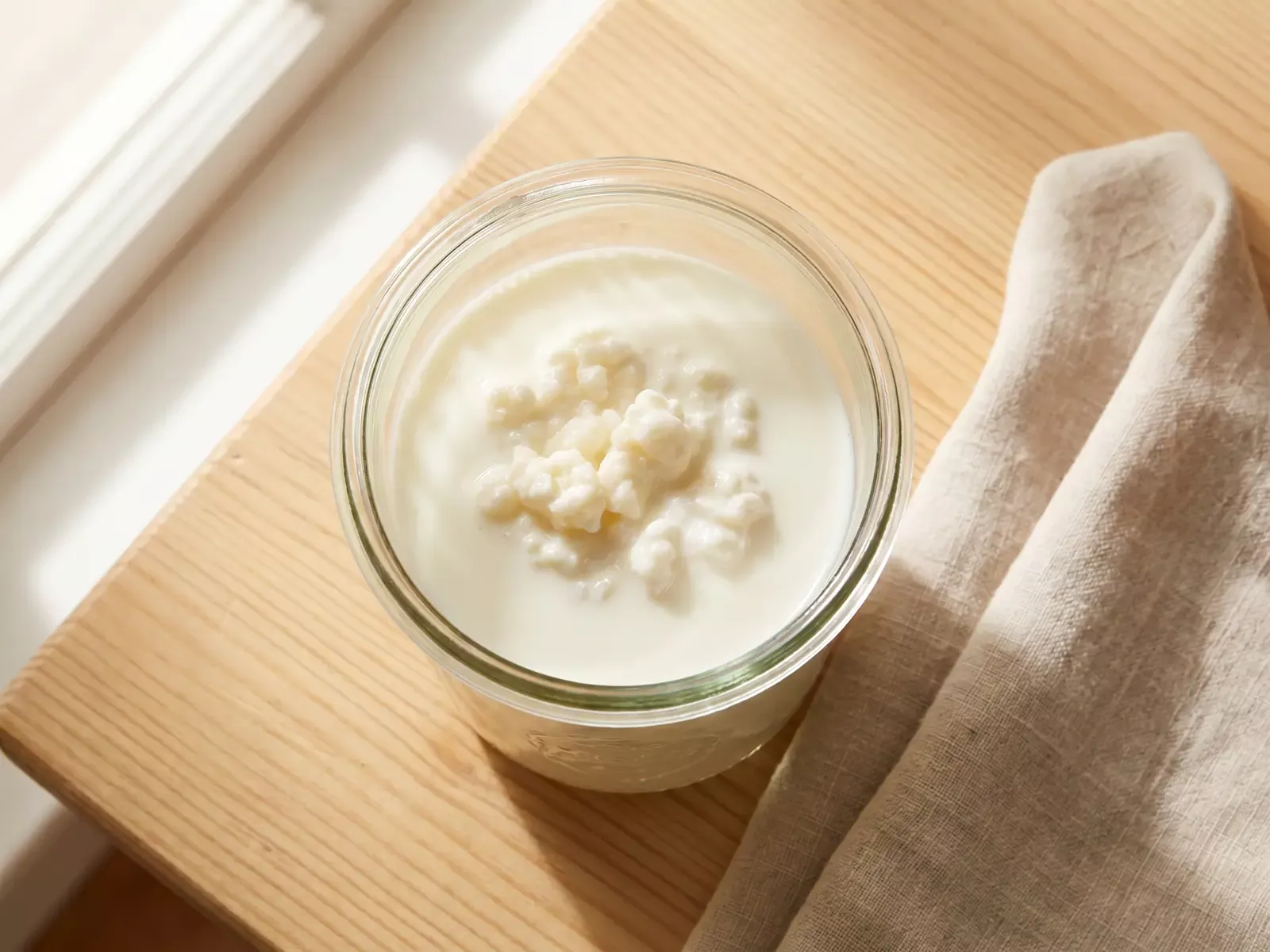 Glazen pot met fermenterende melkkefir naast een linnen doek op een houten ondergrond.