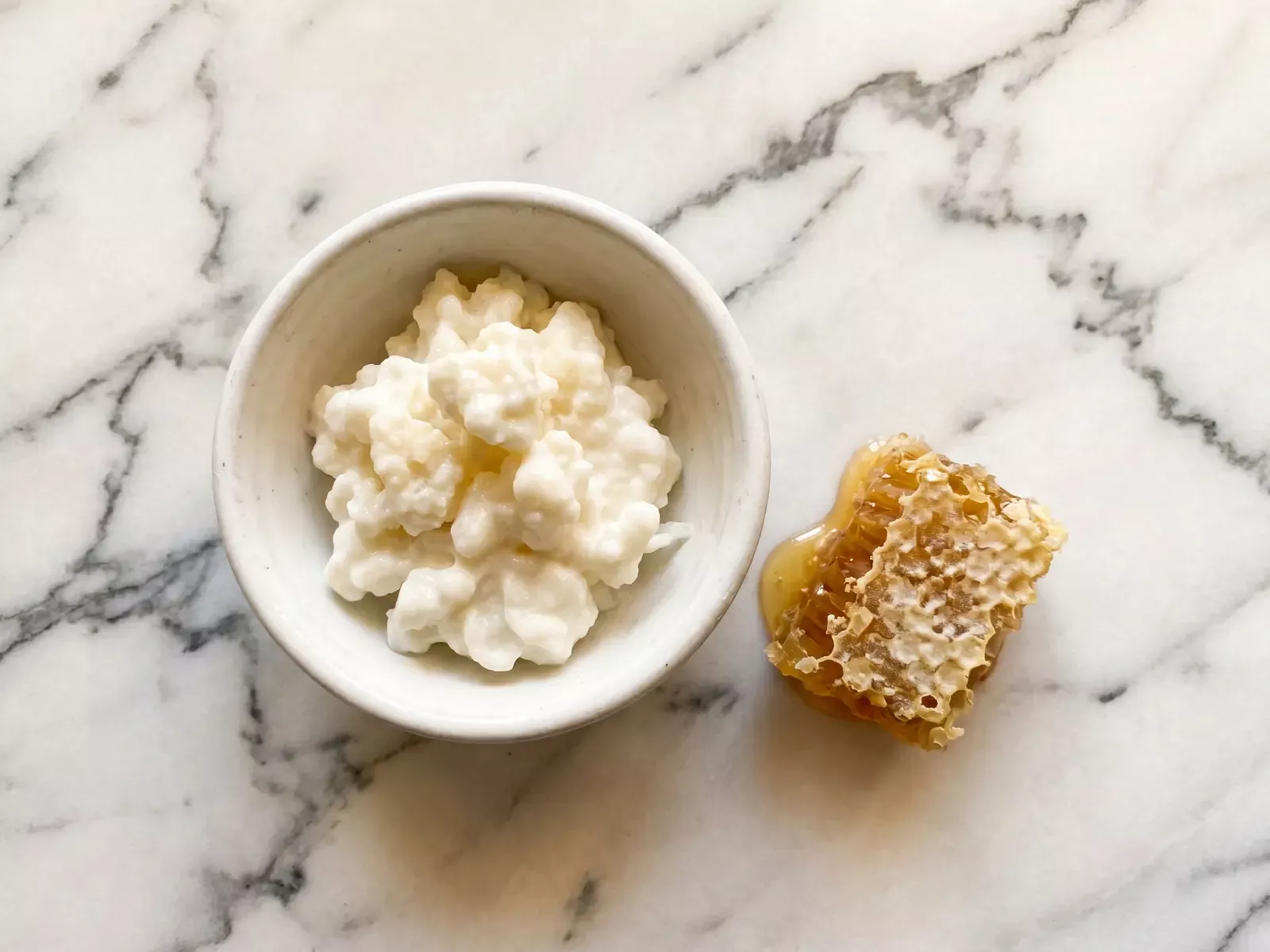 Kom met natuurlijke melkkefir en een stuk honingraat op geaderd marmer onder warm bovenlicht